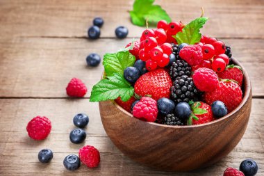 Ahşap arka planda çeşitli yabani böğürtlenli ahşap kase..