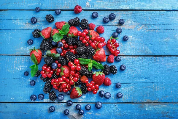 Pile of assorted wild fresh berries on blue wooden background. Top view.