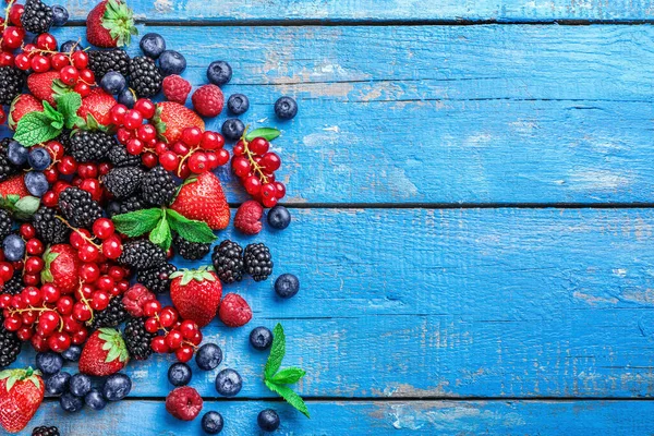 Pile of assorted wild fresh berries on blue wooden background. Top view. Copy space.