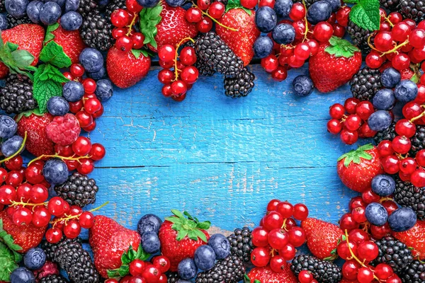 Frame of assorted wild fresh berries on blue wooden background. Top view. Copy space.