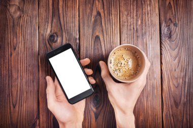 Erkek eller kese kağıdında kahve tutarken ve telefon ahşap arka planda. Üst görünüm.