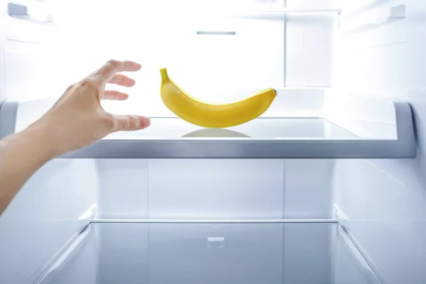 Hand reaching one banana in open empty fridge. Weight loss diet concept.