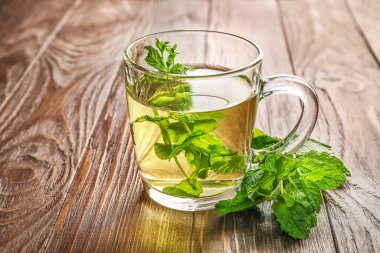Temiz cam bardakta nane çayı ve ahşap zemin üzerinde nane yaprakları..