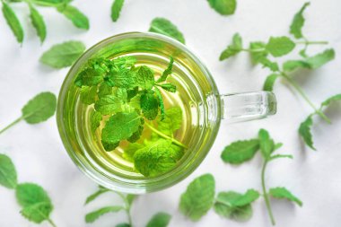 Beyaz zemin üzerinde nane yaprakları olan cam bardakta nane çayı. Üst görünüm.