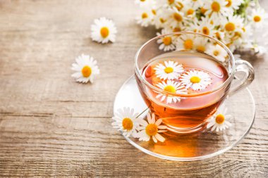 Cam fincanda papatya çayı ve ahşap arka planda çiçek tomurcukları..