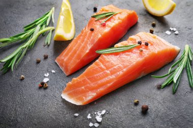 Çiğ somon parçaları, limon dilimleri ve siyah arka planda baharatlar..