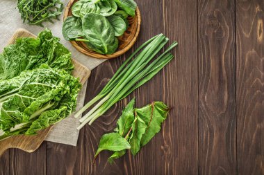 Yeşil sebzeler: ahşap masada soğan, lahana yaprakları, roka, ıspanak ve pazı. Boşluğu kopyala.