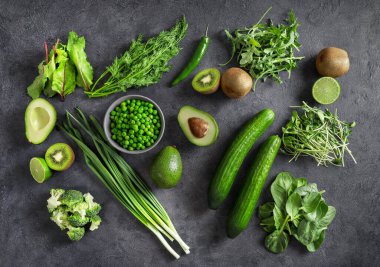 Sağlıklı organik gıdaların üst görüntüsü: salatalıklar, soğanlar, yeşil bezelyeler, brokoli, avokado, kivi meyveleri, limon ve Herbson koyu arka plan. Vejetaryenler için protein kaynağı.