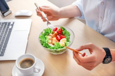 Ofis işyerinde sağlıklı bir iş yemeği. İş adamı, laptopun yanındaki tahta masada sebze ve tavuk salatası yiyor..
