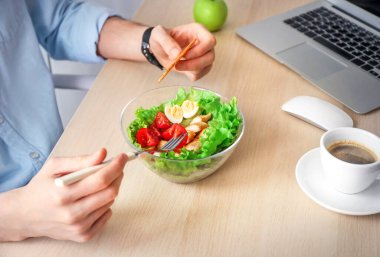Ofis işyerinde sağlıklı bir iş yemeği. İş adamı, laptopun yanındaki tahta masada sebze ve tavuk salatası yiyor..