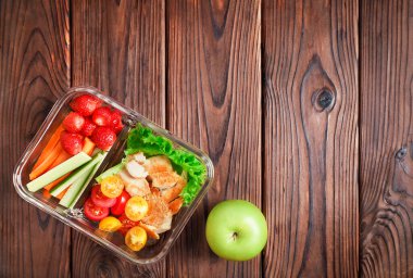 Cam beslenme çantasındaki sağlıklı sebze ve tavuk yemeği ve ahşap arka planda yeşil elma. Üst Manzara. Boşluğu kopyala.