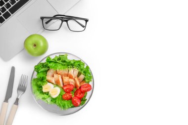 Ofis işyerinde sağlıklı bir iş yemeği. Sebze ve tavuklu salata tabakta ve laptopun ve gözlüklerin yanındaki beyaz masada taze yeşil elma. Boşluğu kopyala.