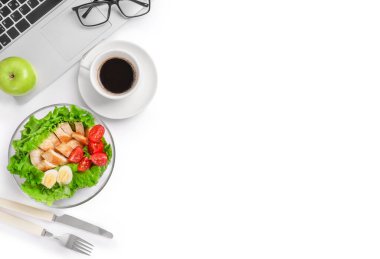 Ofis işyerinde sağlıklı bir iş yemeği. Sebze ve tavuklu salata tabakta, taze yeşil elma ve bir fincan kahve beyaz masada dizüstü bilgisayar ve bardakların yanında. Boşluğu kopyala.