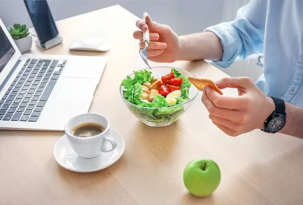 Healthy business lunch in office workplace. Businessman having vegetable and chicken salad in bowl on wooden desk near laptop.