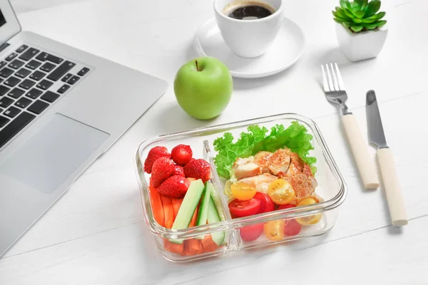 Healthy business lunch in office workplace. Vegetable and chicken salad in lunch box and cup of coffee on white wooden desk near laptop.