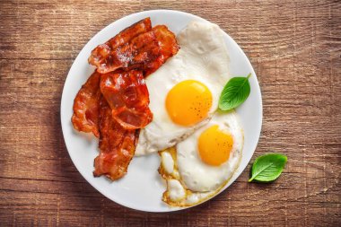 Tam Amerikan kahvaltısı, kızarmış yumurta ve ahşap arka planda kızarmış pastırma. Üst görünüm.