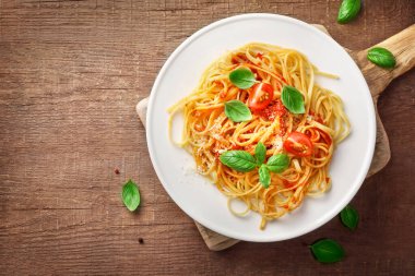 Domatesli İtalyan makarnası, parmezan peyniri ve ahşap arka planda beyaz tabakta fesleğen. Üst görünüm.