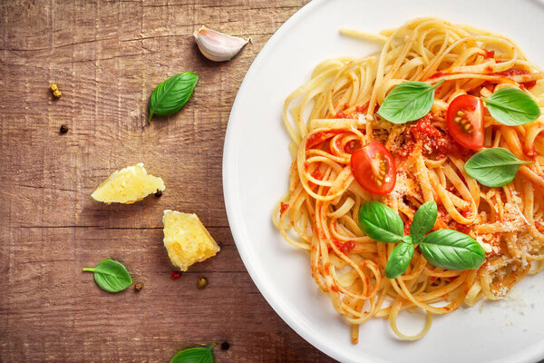 Italian pasta with tomatoes, cheese parmezan and basil on white plate on wooden background. Top view.