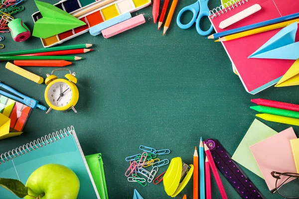 Frame of various school stationery on green blackboard background. Top view. Copy space.