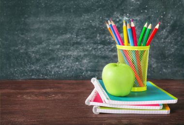 Ahşap masadaki yeşil elma ve okul kırtasiyesi siyah karatahta arka planda. Boşluğu kopyala.