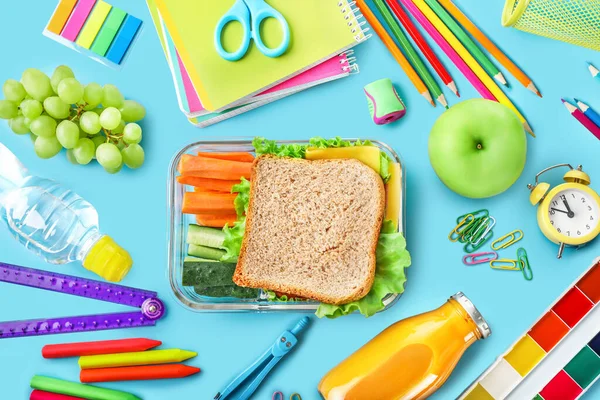 健康的学校午餐盒和各种蓝色背景的学校文具 顶部视图 — 图库照片