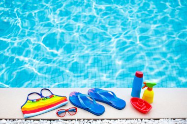 Yüzme havuzu aksesuarları düzdü. Havuz güvertesindeki plaj eşyalarının üst görüntüsü. Parmak arası terlikler, bikini ve şapka, güneş gözlükleri. Su oyuncakları. Tropik tatil beldesinde yaz tatili. Uzayı kopyala Renkli plaj kıyafeti.