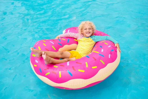 面白い膨らませてドーナツ浮き輪のプール内の子 トロピカル リゾートの屋外プールで泳ぐことを学ぶ少年 子供のためのおもちゃを水します 子供のための健康的なスポーツ活動 太陽の保護 — ストック写真