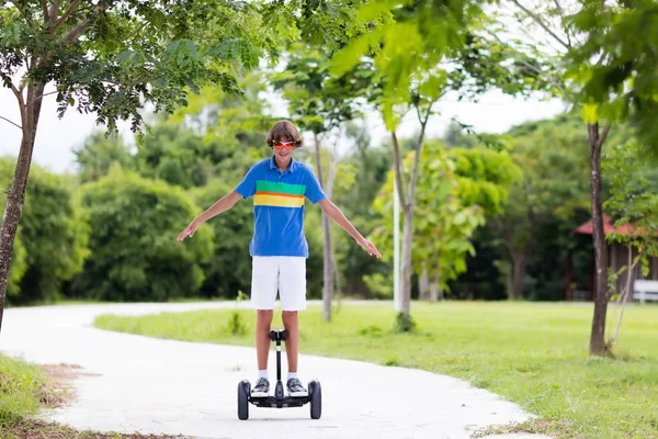 ホバー基板上の子 夏の公園でスクーターに乗る子供 子供のためのバランス ボード 電気釣り合っている都市通りのスクーター ホバーボードに乗ることを学ぶの少年 学校の子供のための現代的なガジェット — ストック写真