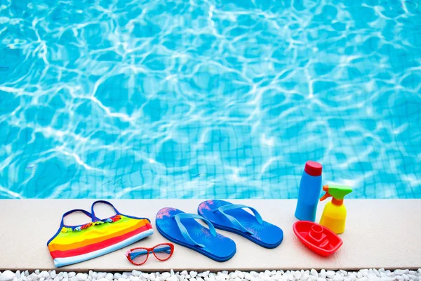 Swimming pool accessories flat lay. Top view of beach items on pool deck. Flip flops, bikini and hat, sun glasses. Water toys. Summer vacation in tropical resort. Copy space. Colorful beach wear.