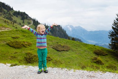 Alp dağlarında yürüyüş yapan çocuklar. Çocuklar Avusturya 'da karla kaplı dağa bakıyorlar. Bahar tatili. Küçük çocuk çayırlarda yürüyüş parkurunda. Açık hava eğlencesi ve sağlıklı aktivite.