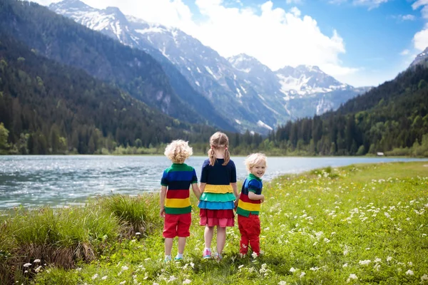 孩子们在阿尔卑斯山上徒步旅行 看着美丽的湖泊 孩子在高山花卉领域在雪盖的山在奥地利 春天的家庭假期 女孩和男孩在徒步旅行路线 户外娱乐 — 图库照片