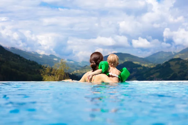 母亲和婴儿在阿尔卑斯山日落的豪华温泉高山度假胜地的室外无限游泳池中玩耍 与孩子们一起度过春天或暑假 家庭与孩子在热的浴缸与山看法 — 图库照片