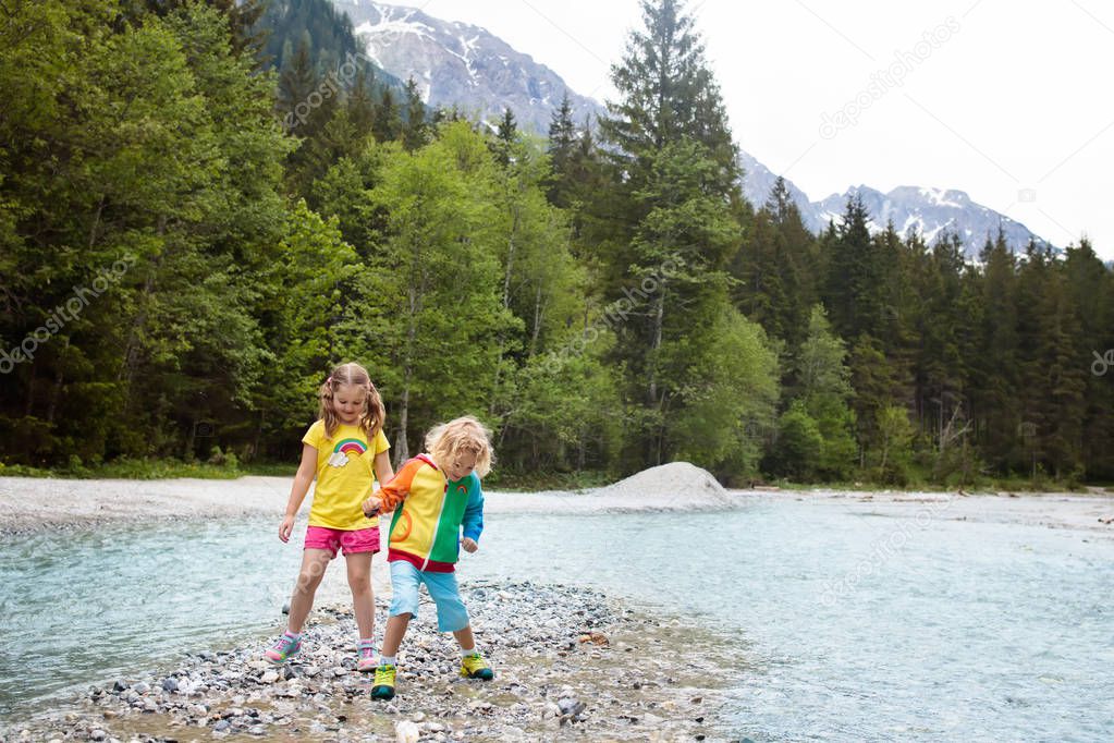 Children hiking in Alps mountains crossing river. Kids play in water at mountain in Austria. Spring family vacation. Little boy and girl on hike trail. Outdoor fun. Active recreation with children.