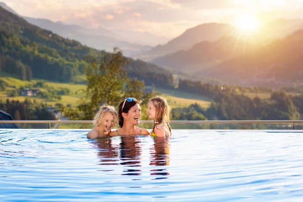 在奥地利阿尔卑斯山的豪华温泉高山度假胜地 母亲和孩子们在室外的无限大游泳池里玩耍 有子女家庭的春假或暑假 在有山景的热浴缸里的孩子 — 图库照片