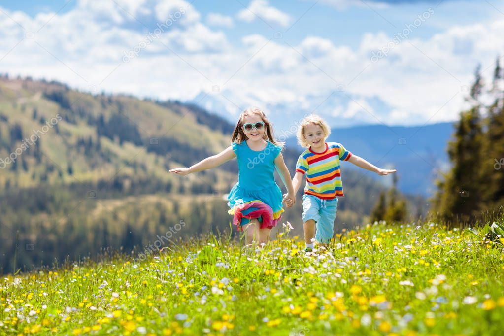 Children hiking in Alps mountains. Kids run at snow covered mountain in Austria. Spring family vacation. Little boy and girl on hike trail in blooming alpine meadow. Outdoor fun and healthy activity