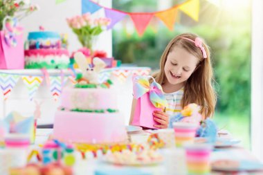Doğum günü partisi renkli gökkuşağı pastel dekorasyon ve bunny katman pasta ile çocuklar. Küçük kız tatlı, şeker ve meyve ile. Balonlar ve afiş çocuk veya Bebek Doğum günü için şenlikli bir şekilde dekore edilmiş masada.