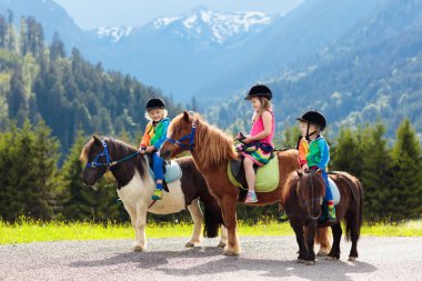 Alp Dağları'nda midilli sürme çocuklar. At çiftliği Avusturya, Tirol aile bahar tatil. Çocuklar ata binmek. Hayvan bakımı çocuk. Çocuk ve evde beslenen hayvan. Küçük kız ve midilli eyer çocuk.