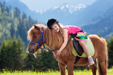 Alp dağlarında midilliye binen çocuklar. Avusturya 'daki at çiftliğinde aile tatili, Tirol. Çocuklar ata biner. Çocuk hayvanla ilgileniyor. Çocuk ve evcil hayvan. Çiçek açan çayırdaki küçük kız.