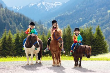 Alp Dağları'nda midilli sürme çocuklar. At çiftliği Avusturya, Tirol aile bahar tatil. Çocuklar ata binmek. Hayvan bakımı çocuk. Çocuk ve evde beslenen hayvan. Küçük kız ve midilli eyer çocuk.