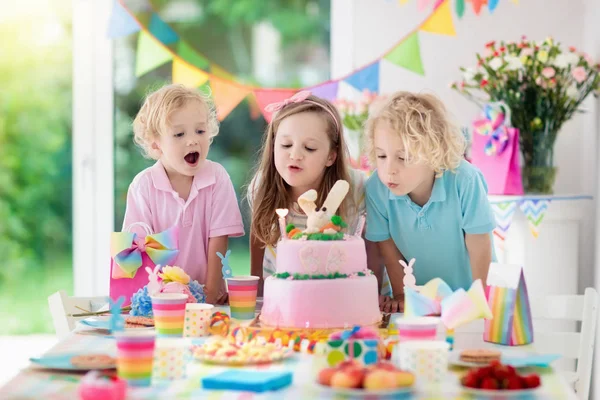 子供の誕生日パーティー 子どもたちはピンクのバニー ケーキのろうそくを吹き消します パステルの虹の装飾と子供たちのイベント バナー フラグはテーブルセッティング 女の子と男の子の誕生日プレゼントに 家族のお祝い — ストック写真