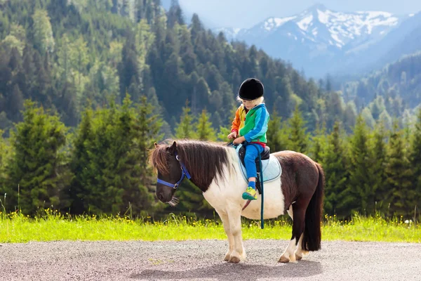 孩子们骑着小马在阿尔卑斯山里在奥地利蒂罗尔的马场度过家庭春假 孩子们骑马 孩子照顾动物 孩子和宠物 骑在马上的小男孩 — 图库照片