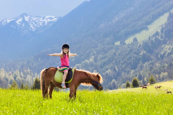 Alp dağlarında midilliye binen çocuklar. Avusturya 'daki at çiftliğinde aile tatili, Tirol. Çocuklar ata biner. Çocuk hayvanla ilgileniyor. Çocuk ve evcil hayvan. Çiçek açan çayırdaki küçük kız.