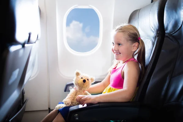 飛行機内の子 飛行機の窓側の席に座っているは子供します 子供のための機内エンターテインメント 連れのお客様 子供は飛ぶし 旅行します 家族の夏休み 飛行機のおもちゃを持つ少女 — ストック写真