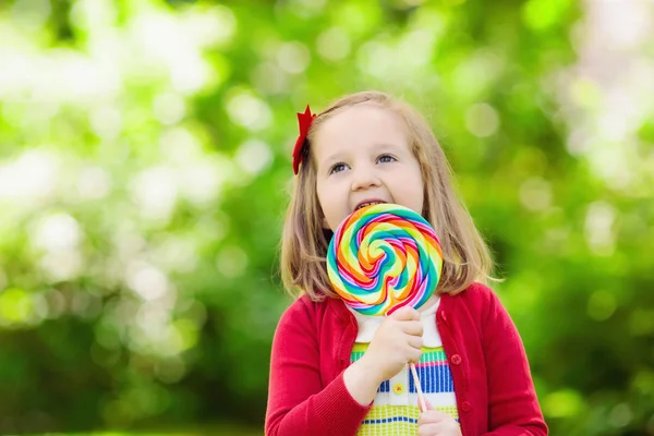 大きなカラフルなロリポップでかわいい女の子 子供食べる甘いお菓子バー 若い子供のためのお菓子 夏の屋外の楽しみ 砂糖キャンディーと未就学児の子供 子供の幼稚園後公園にスナックがあります — ストック写真