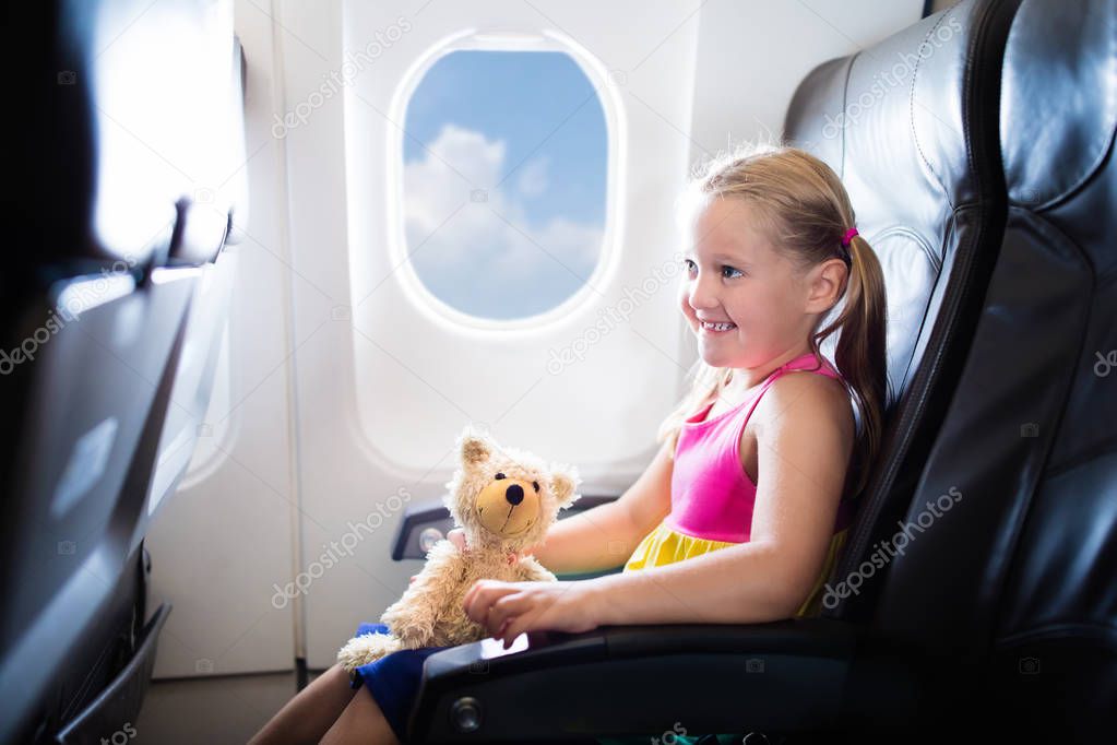 Child in airplane. Kid in air plane sitting in window seat. Flight entertainment for kids. Traveling with young children. Kids fly and travel. Family summer vacation. Girl with toy in airplane.