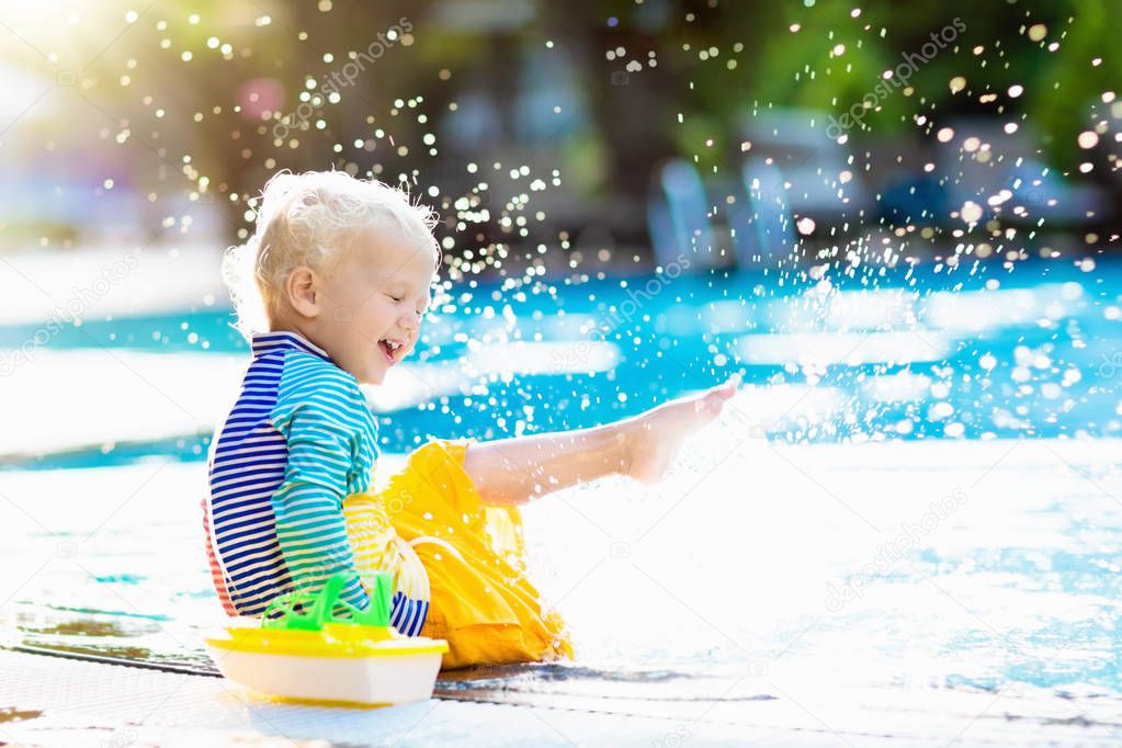 Baby with toy boat in swimming pool. Little boy learning to swim in outdoor pool of tropical resort. Swimming with kids. Healthy sport activity for children. Sun protection swim wear. Water toys.