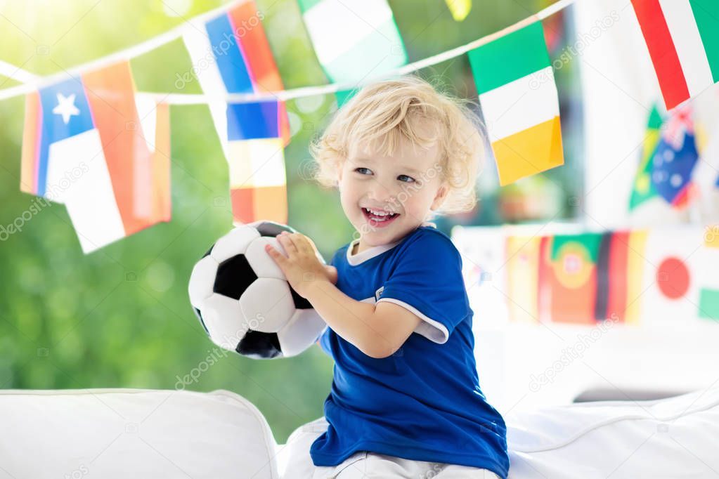 Child watching football game on tv. Little boy in France tricot watching soccer game during championship. Kid fan cheering and supporting national team. Young football player with ball before match.