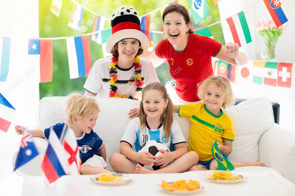 Family with children watching football game on television. Group of young adults and kids in national tricot watch soccer match on tv. Fans cheering and supporting country team at championship.