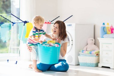 Anne ve çocuklar Çamaşırhane, çamaşır makinesi ile Oda veya kurutma. Aile işleri. Modern ev aygıtları ve çamaşır deterjan beyaz güneşli evinde. Raf kurutma üzerinde temiz yıkanmış kıyafetler. 