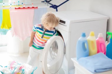 Çocuk Çamaşırhane, çamaşır makinesi ile Oda veya kurutma. Çocuk ile aile işleri yardımcı. Modern ev aygıtları ve çamaşır deterjan beyaz güneşli evinde. Raf kurutma üzerinde temiz yıkanmış kıyafetler. 